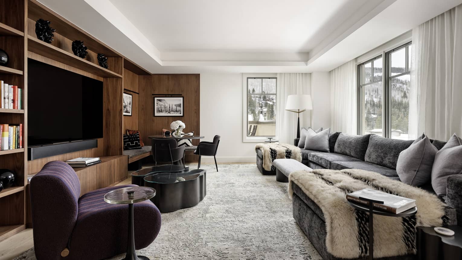 Contemporary, light-filled living room with large grey sofa, plum arm chair and built-in wooden media centre