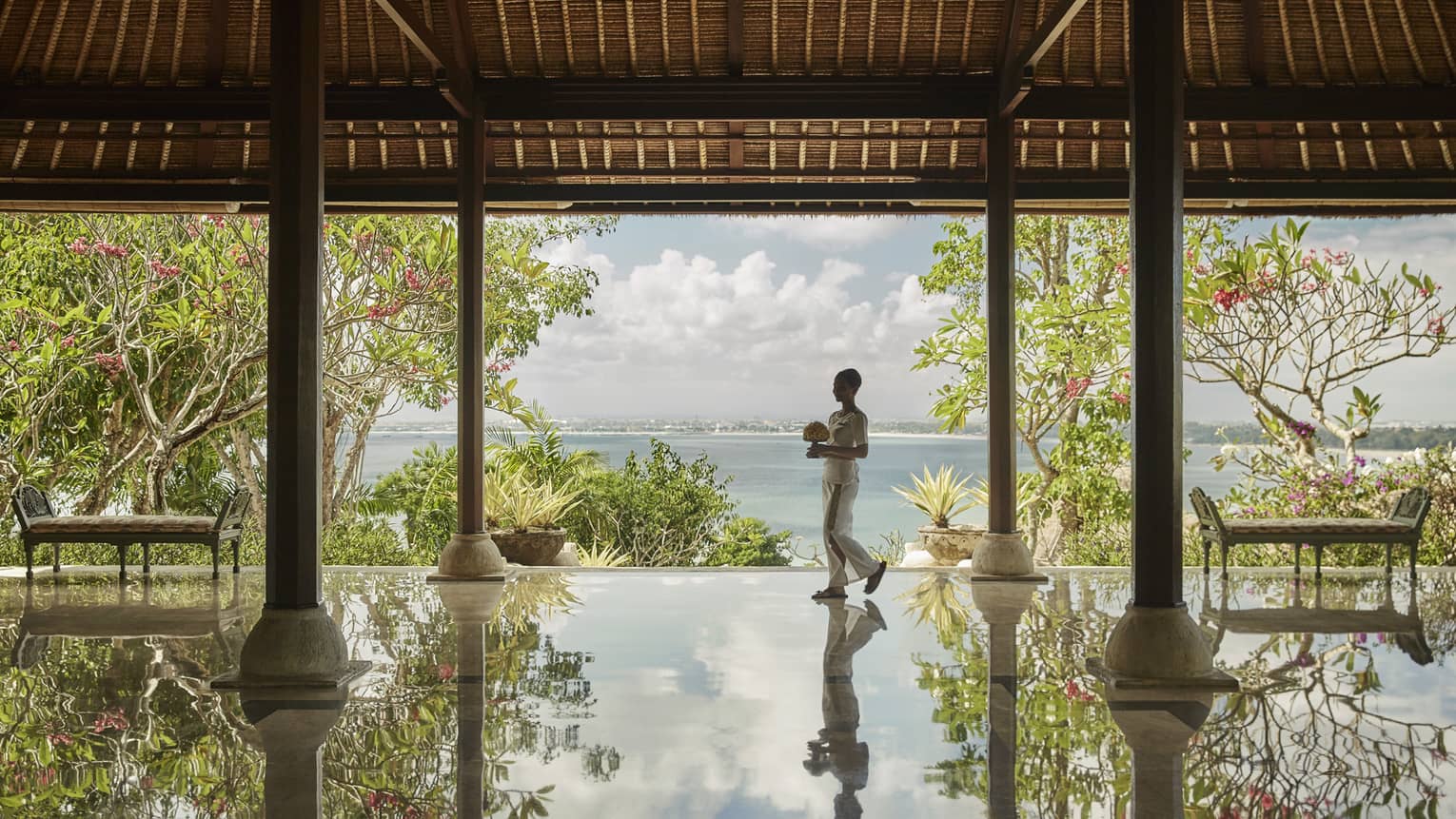 Hotel staff carrying flowers reflected onto floor of open-air pavilion