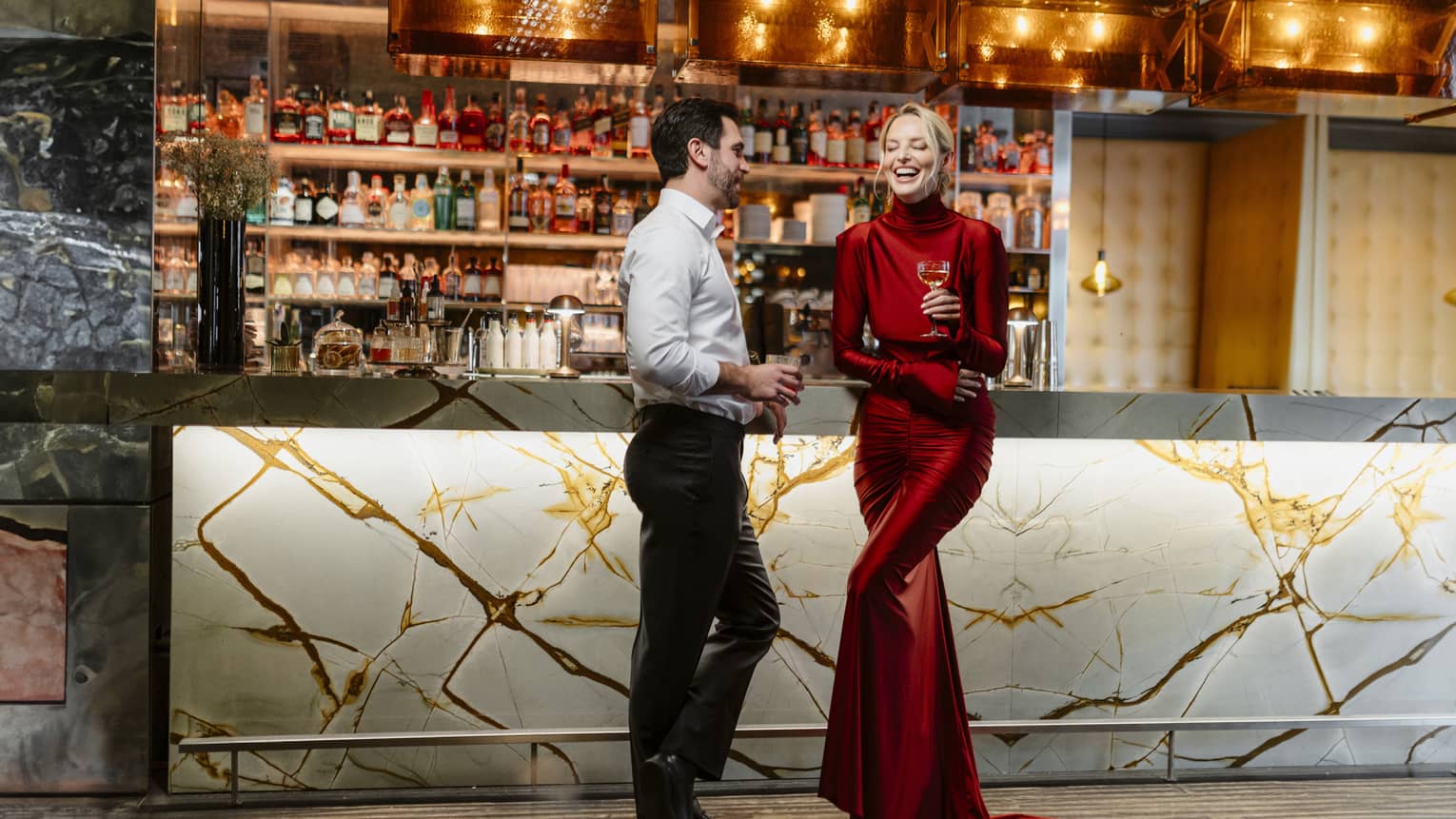 Couple standing, laughing in front of a dimly lit stocked bar