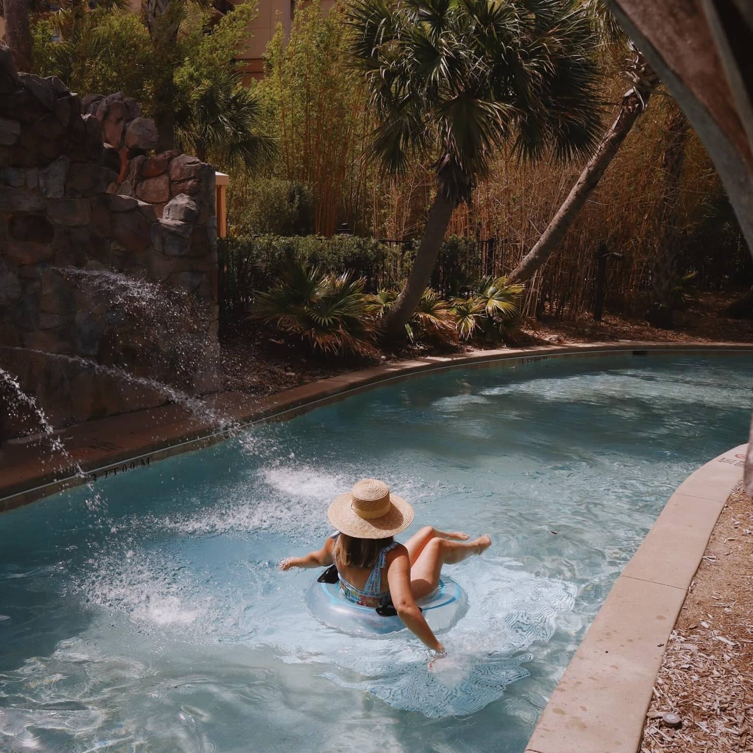 A woman in a swimsuit and sunhat floats on a lazy river in a tube