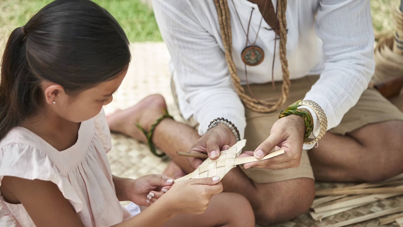 An adult shows a young girl how to weave a basket