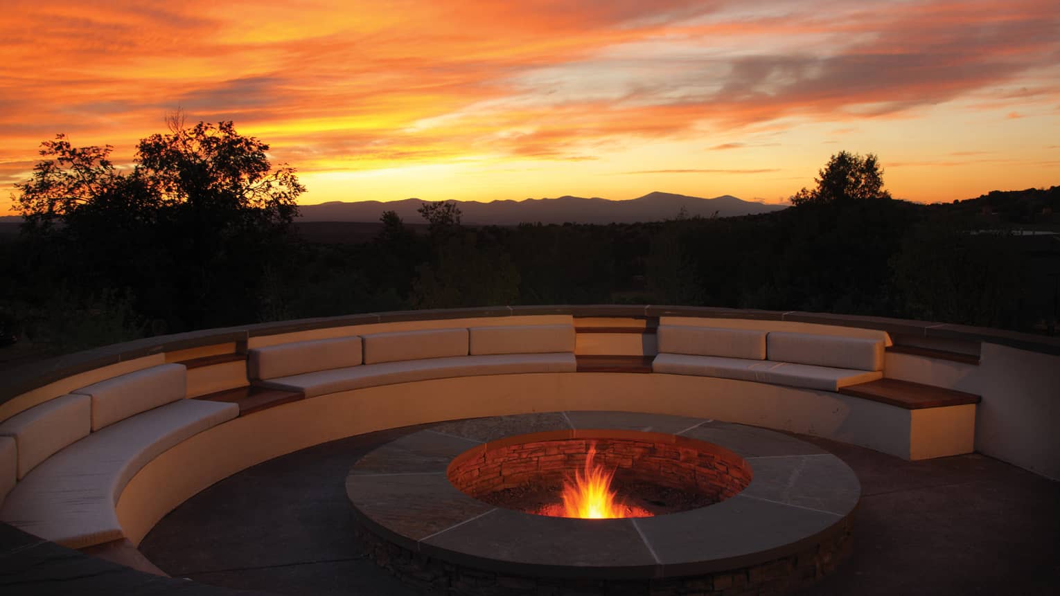 Outdoor fire pit burning with a large curved sofa, colourful sunset in the sky