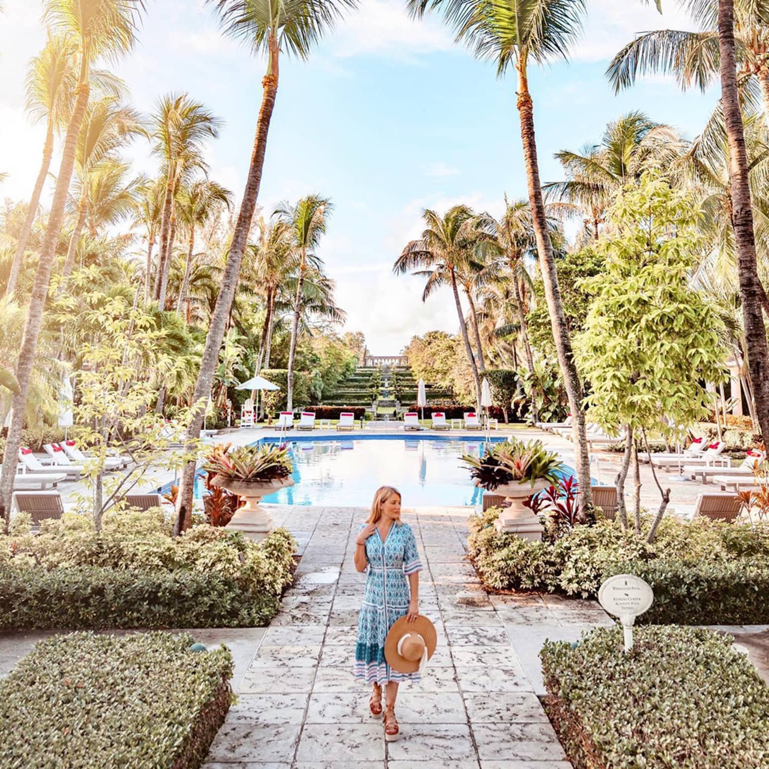 Person walking by a pool surrounded by palm trees at a Four Seasons tropical resort under a bright, sunny sky
