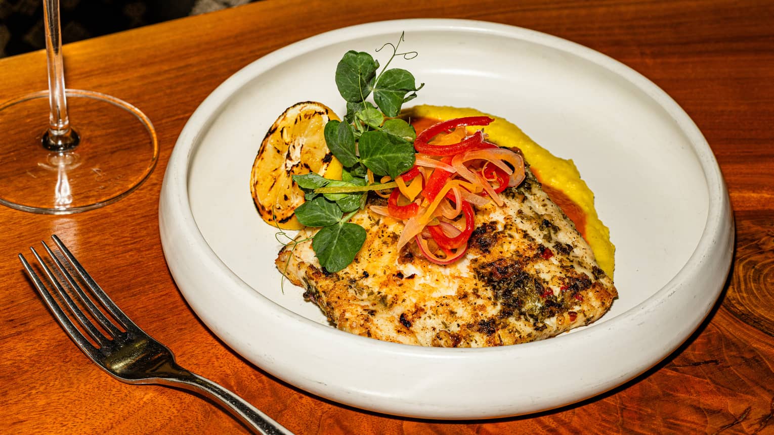 A round, white, shallow bowl on a wood table holds colourful food items.