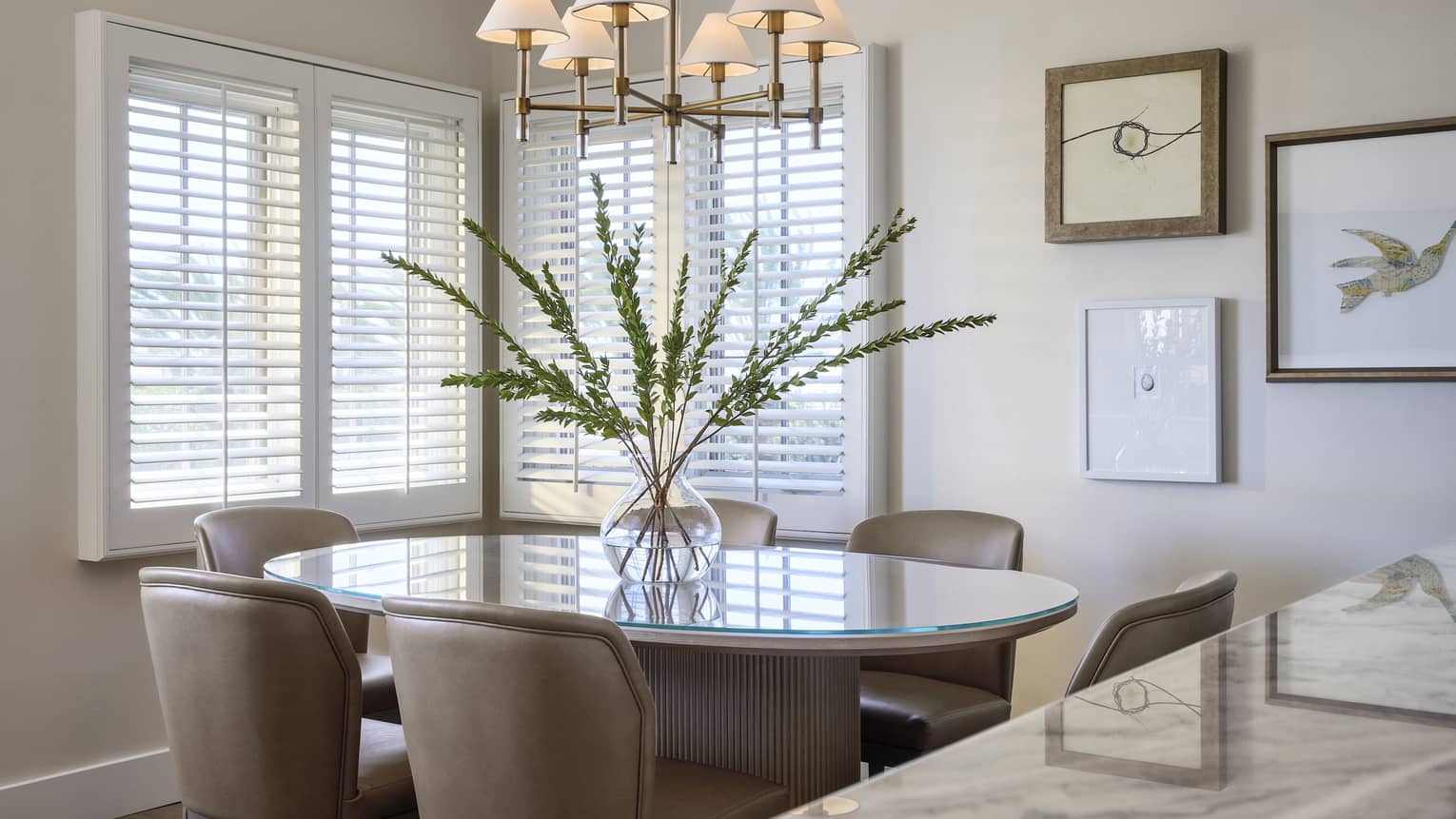 Elegant dining room in villa, with six chairs, large floral arrangement, and white shutter blinds on windows