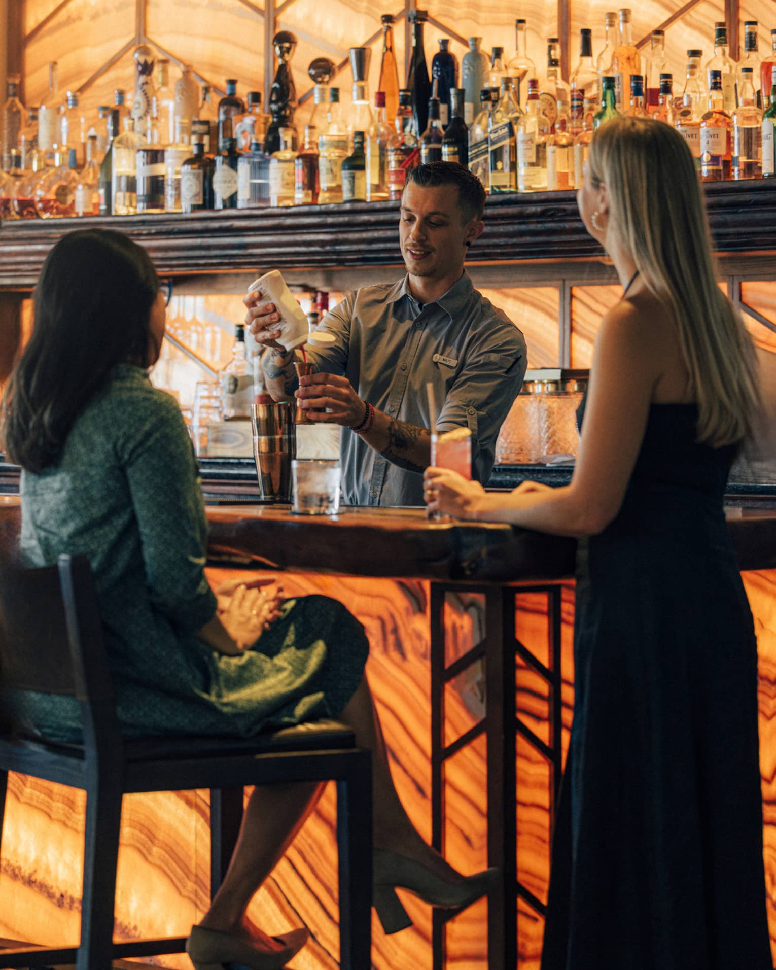Two guests at the bar while the bartender is making a drink.