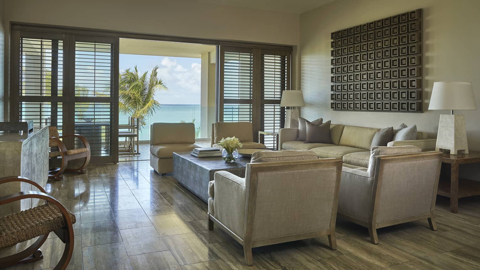 Bright living room with beige armchairs, sofa and ocean-view terrace framed by palm trees