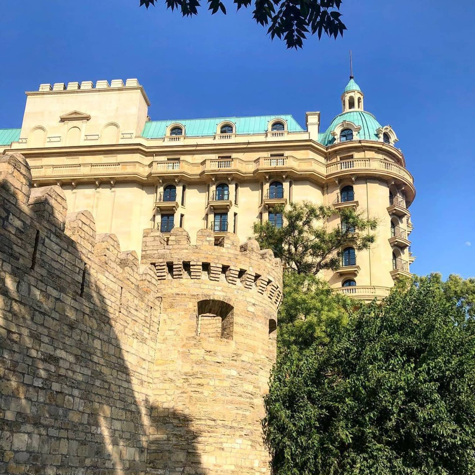 A sunlit view of the hotel exterior underneath a bright blue sky, surrounded by foliage