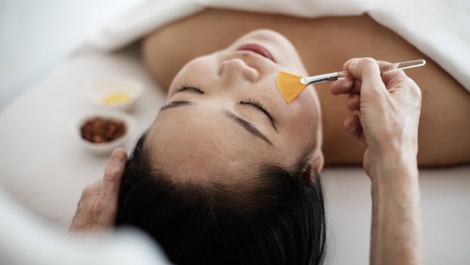 A woman receiving a spa treatment utilizing a brush on her face.