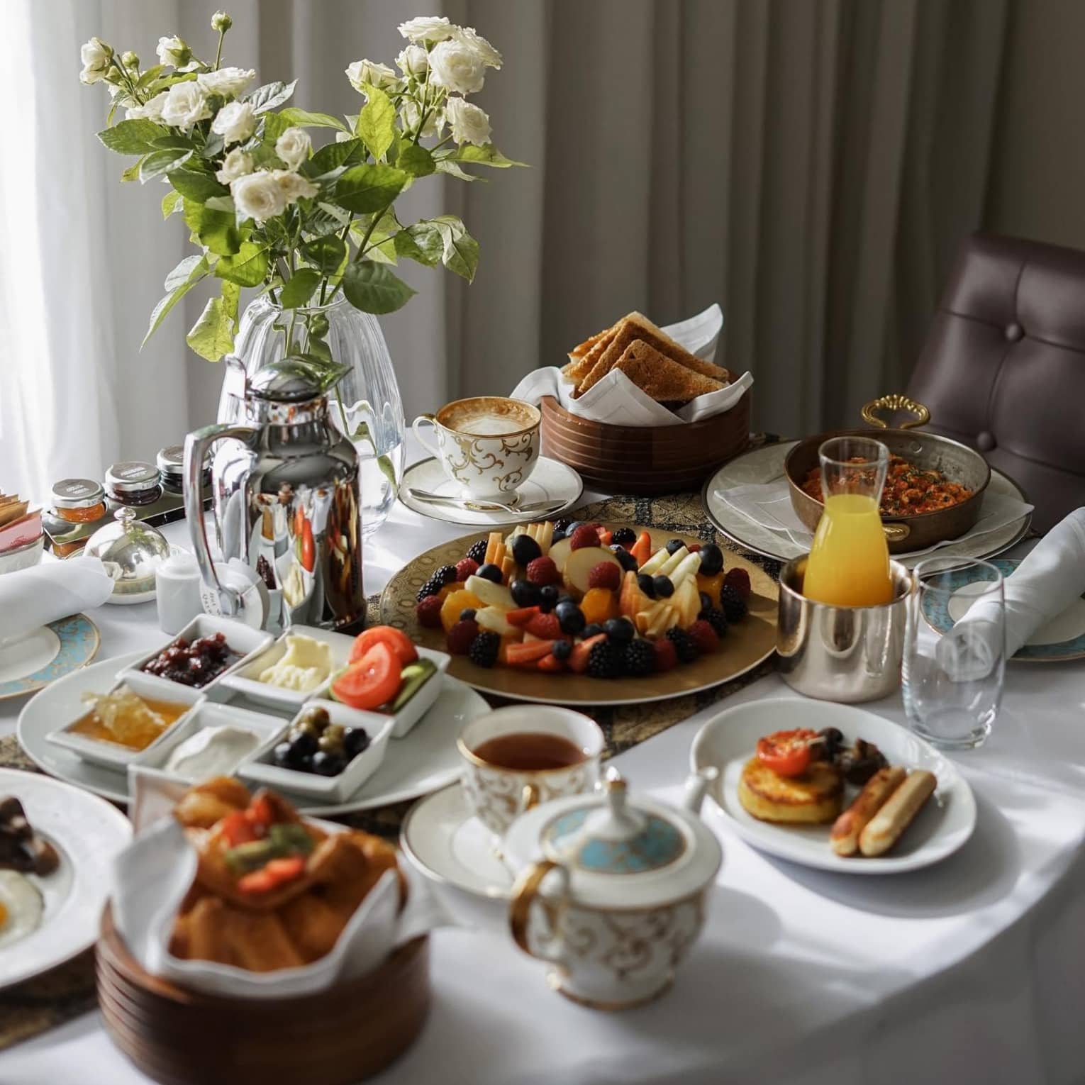 Plates of breakfast food, tea, juice and a floral arrangement sit on a table covered by a white tablecloth