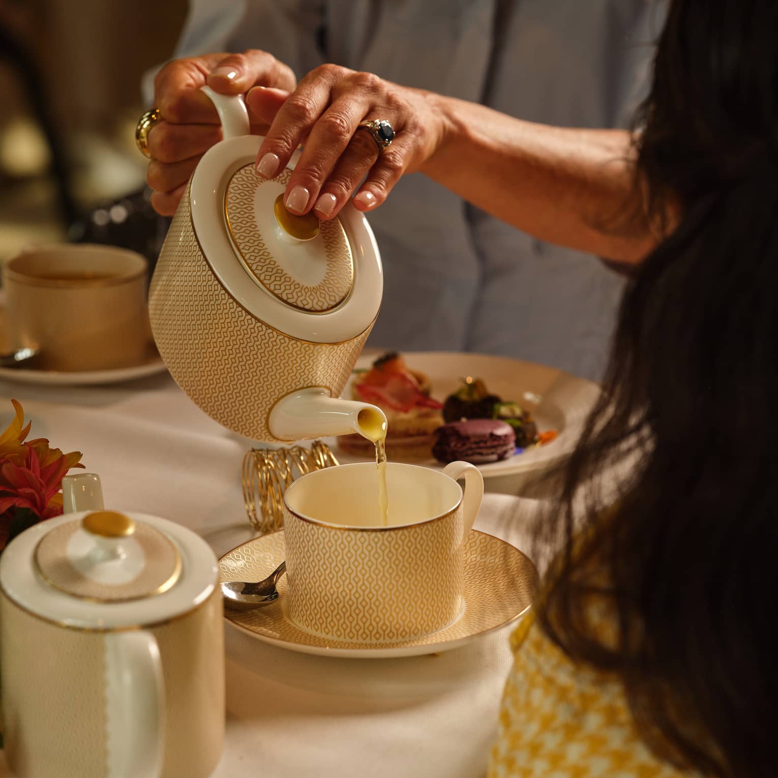 Person pours tea from a cream porcelain tea pot into a matching mug