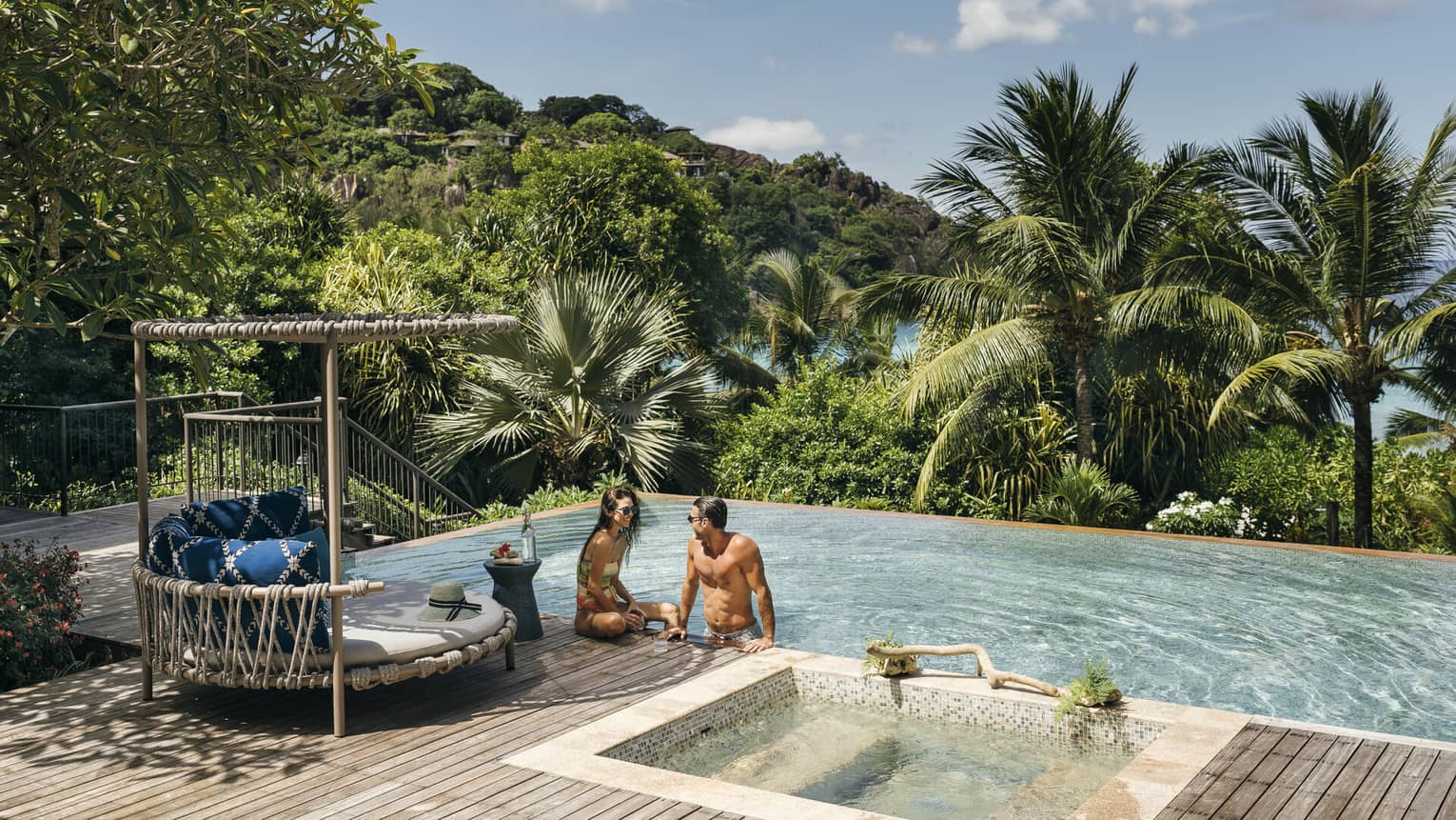 A couple sits by a large infinity pool overlooking the ocean
