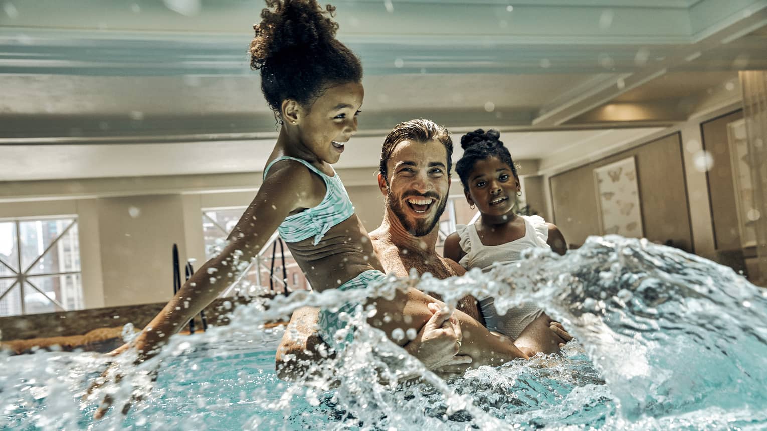 A father playing with his daughters in a pool.