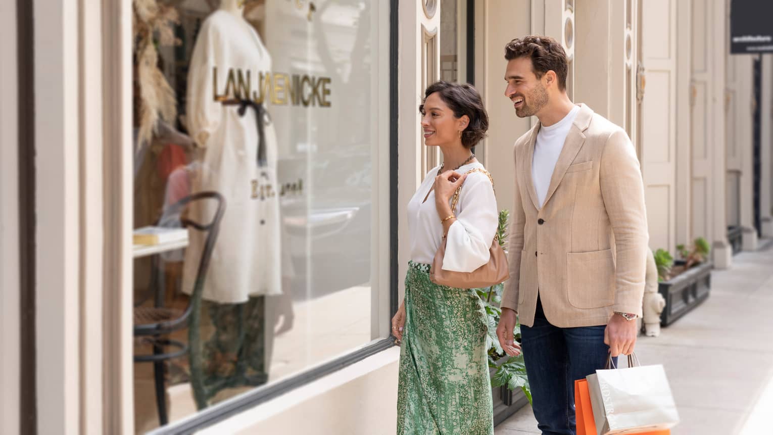 Two people smiling while window shopping in front of a boutique store.