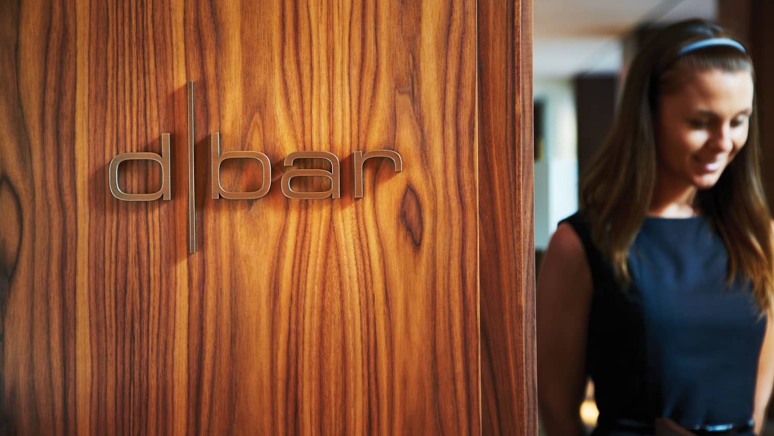 Woman walks through doorway beside wood wall with Dbar sign