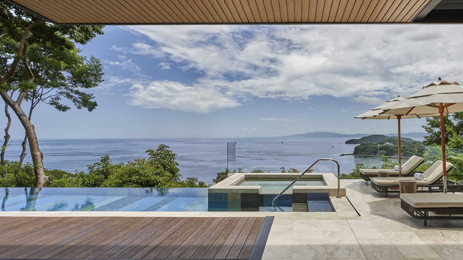 Private villa pool deck with cushioned lounge chairs, hot tub and sea view