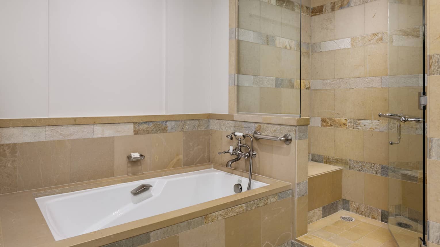 Hotel bathroom with beige stone tile, a soaking tub and a glass-enclosed walk-in shower with a bench