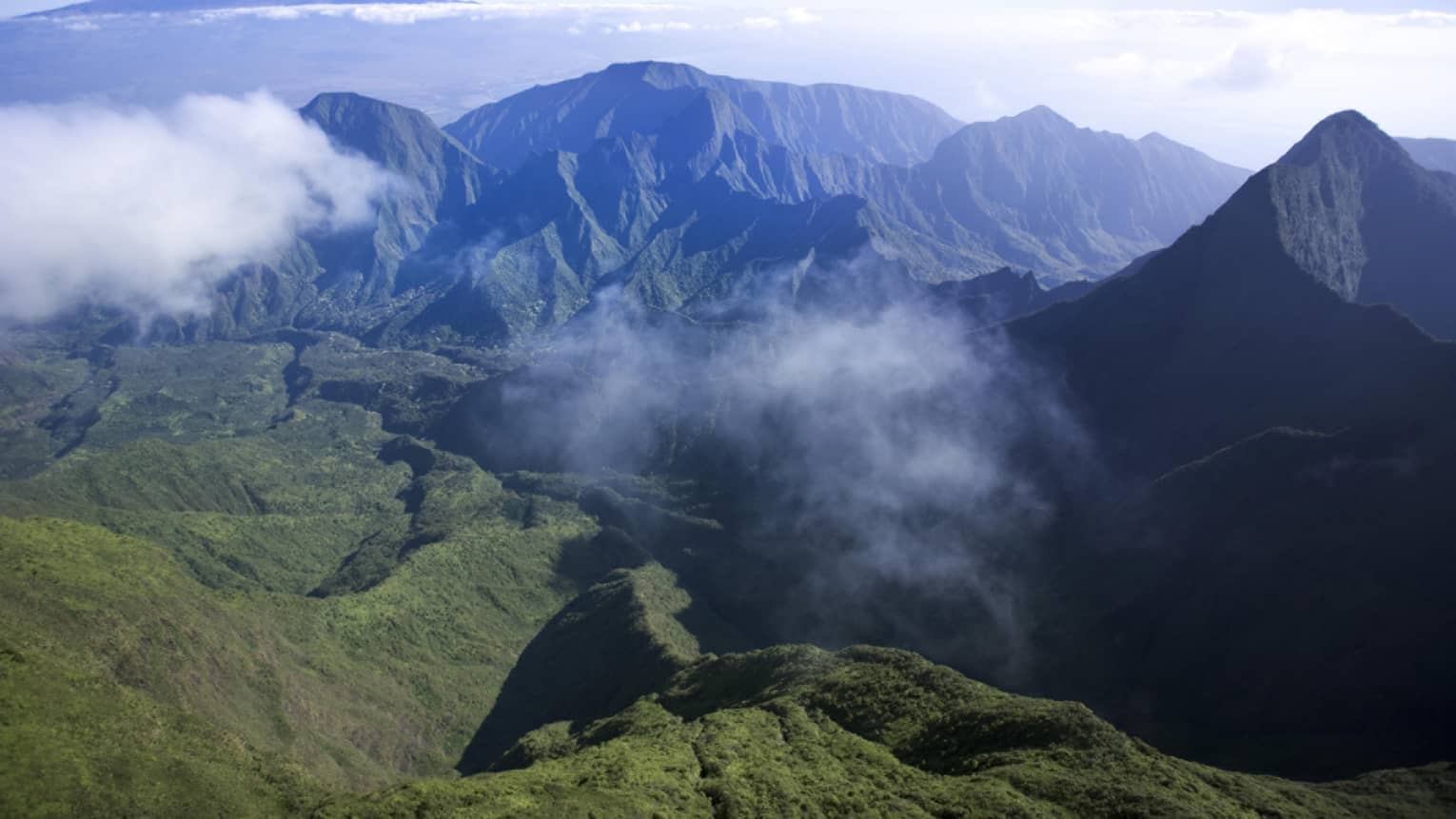 Clouds hover over green volcanic mountains