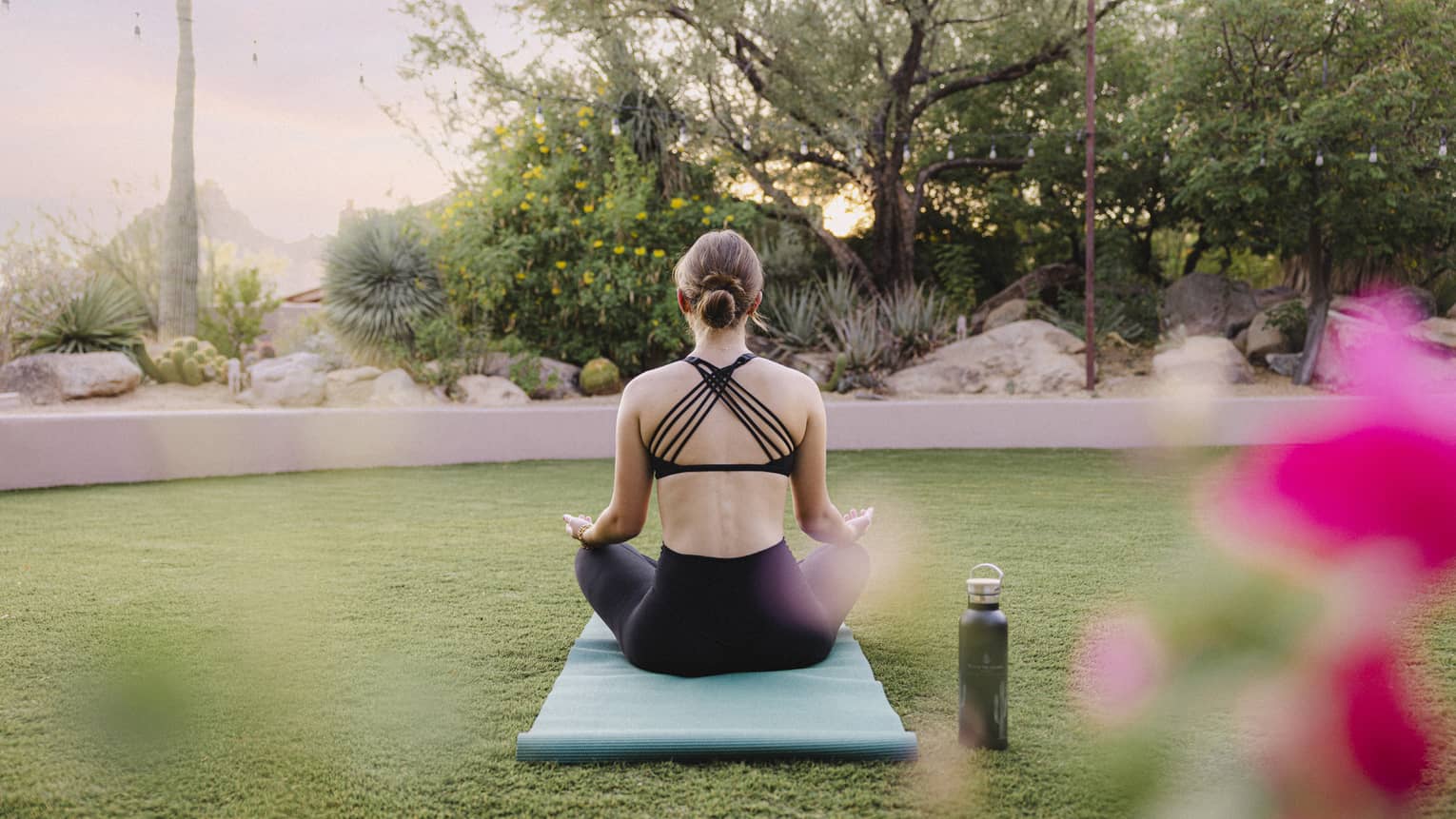 Person doing yoga outside on a blue yoga mat with a water bottle beside them.
