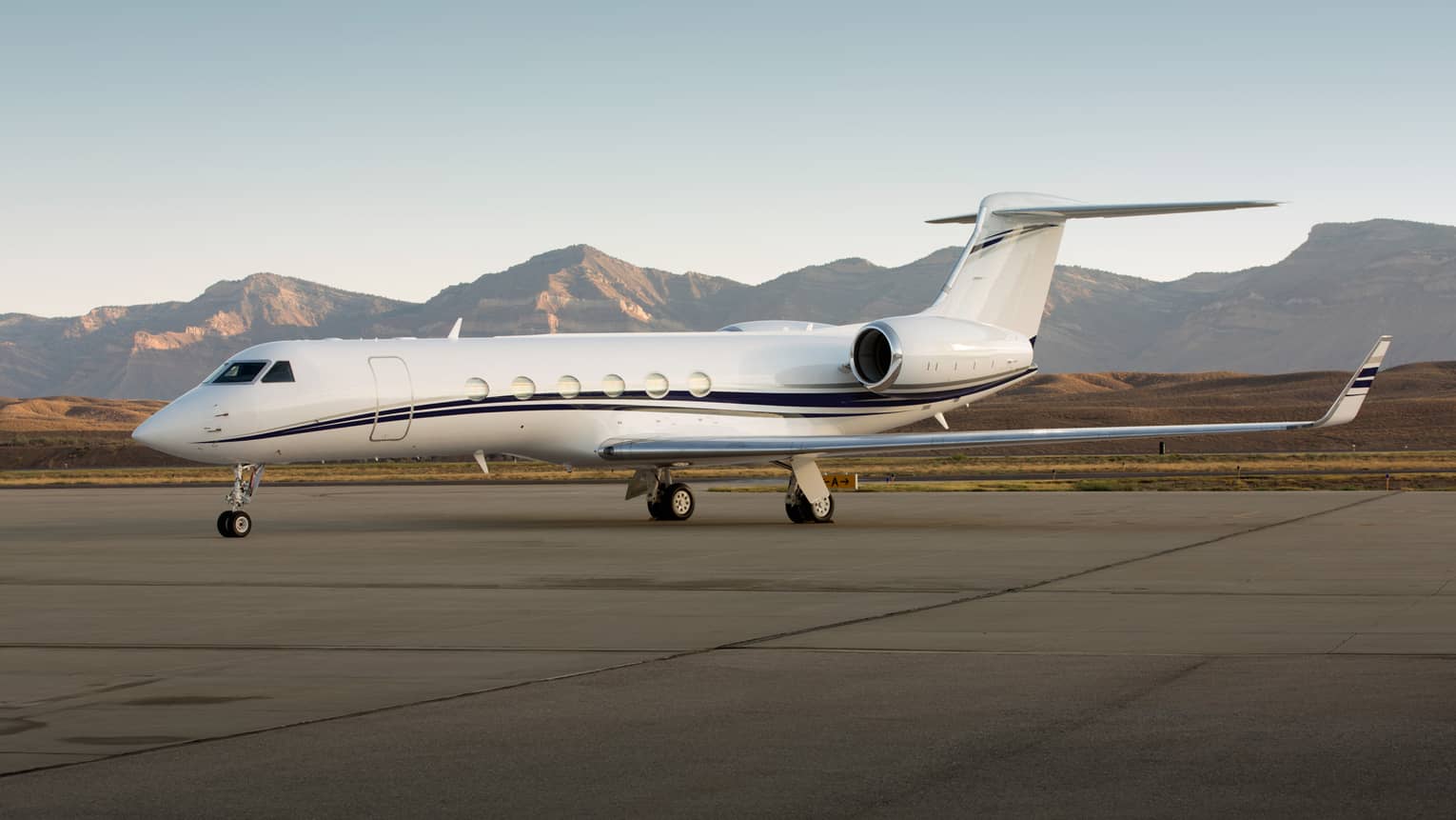 Private jet parked on a runway with mountain range in the background.