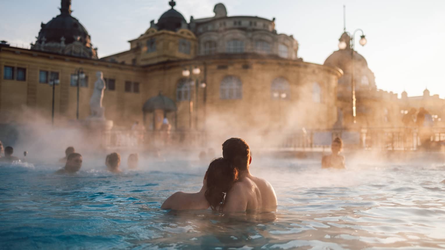 Couple huddled together in thermal pool at Szechenyi Thermal Baths in Budapest, other bathers in background