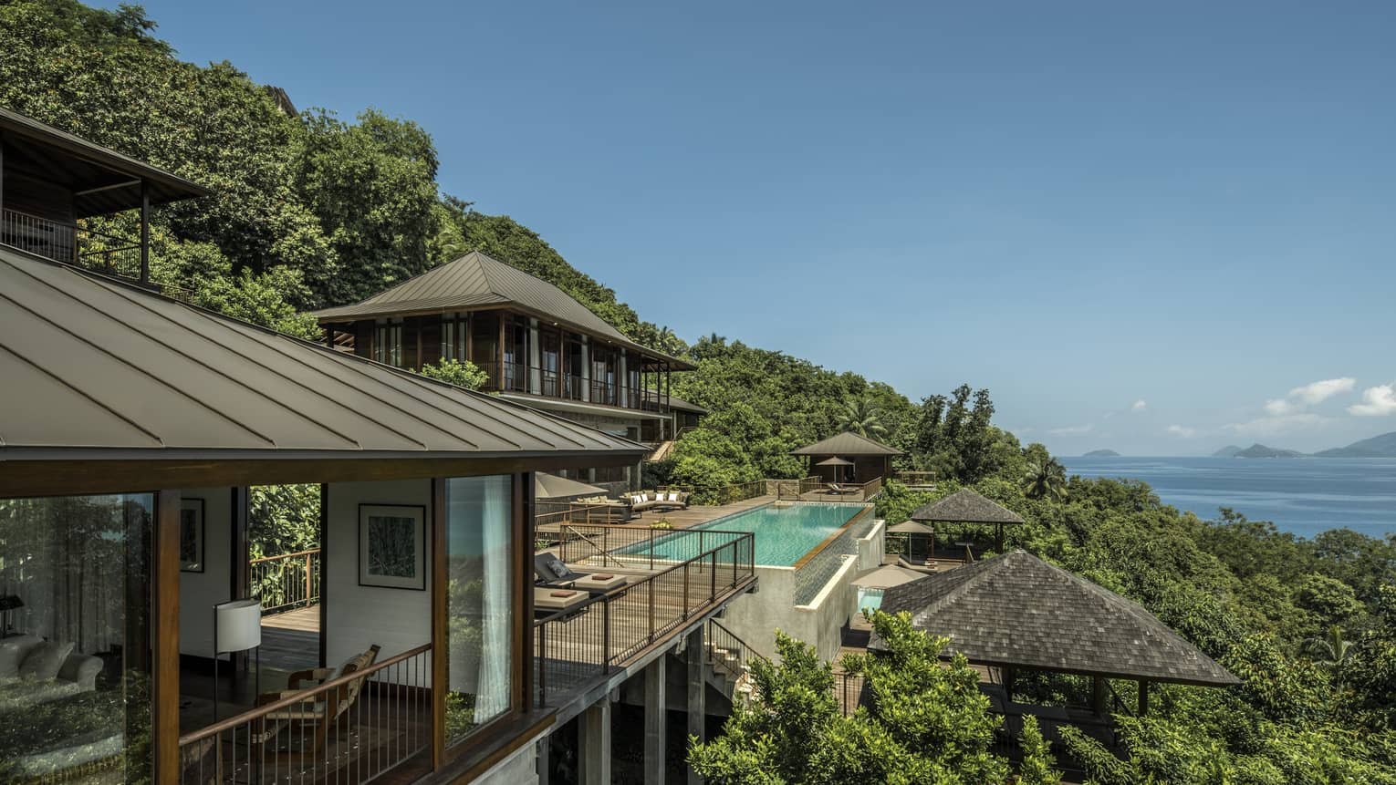 Four-Bedroom Residence Villa roofs, patios amid trees on mountain, ocean below