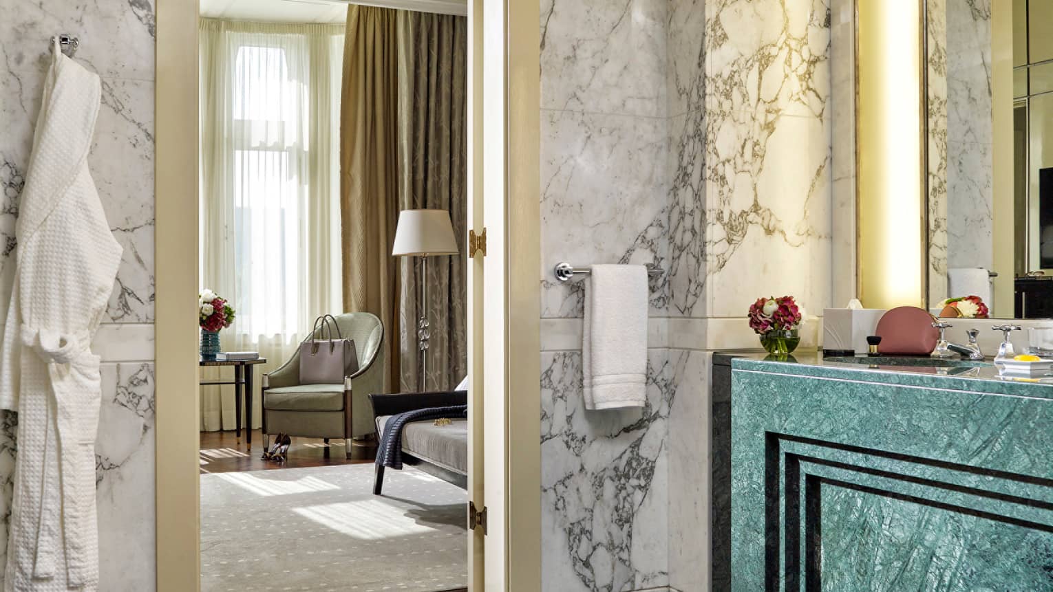 Luxurious marble bathroom with green vanity and view into a sunlit hotel bedroom