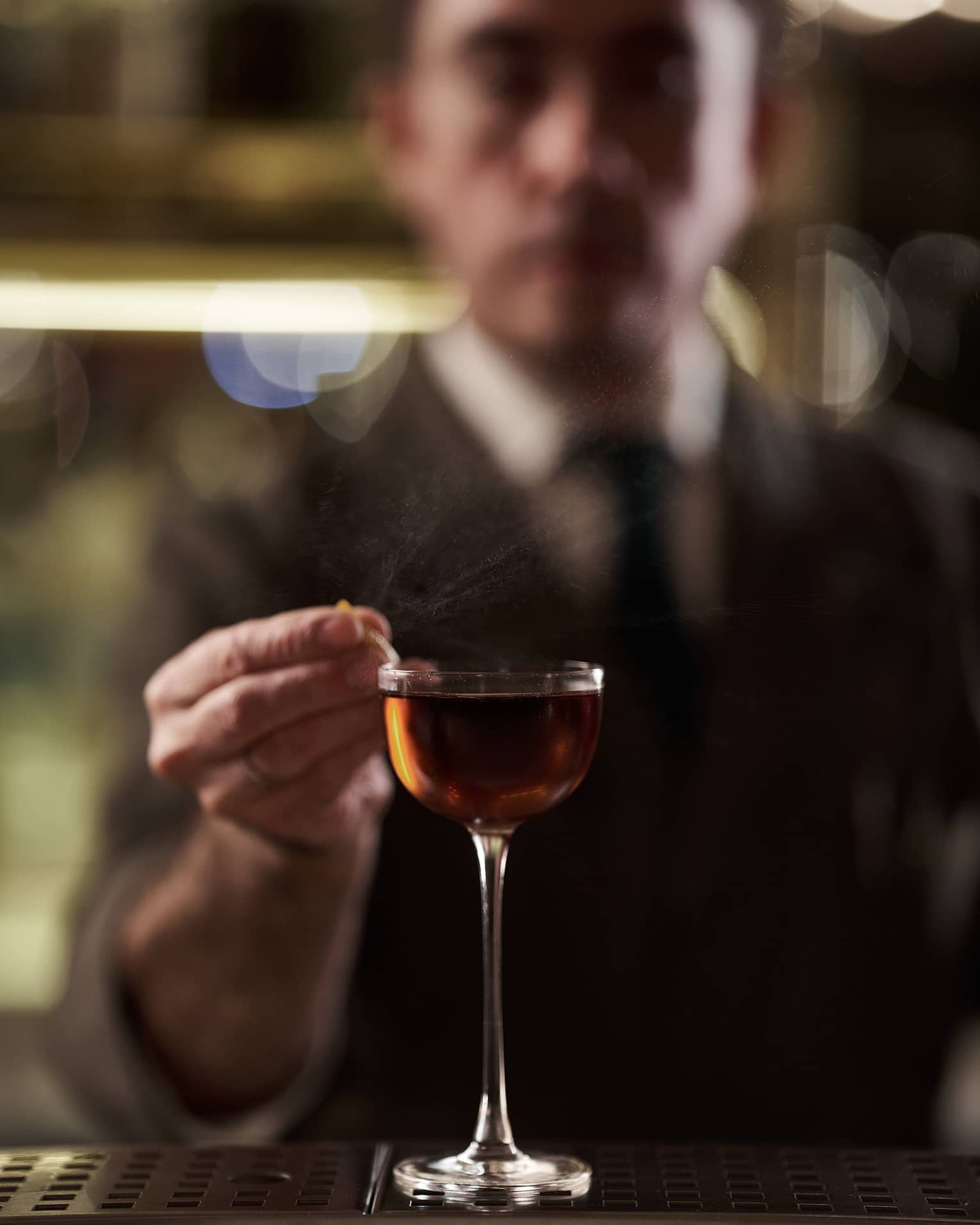Bartender in suit garnishing a tall amber-coloured cocktail