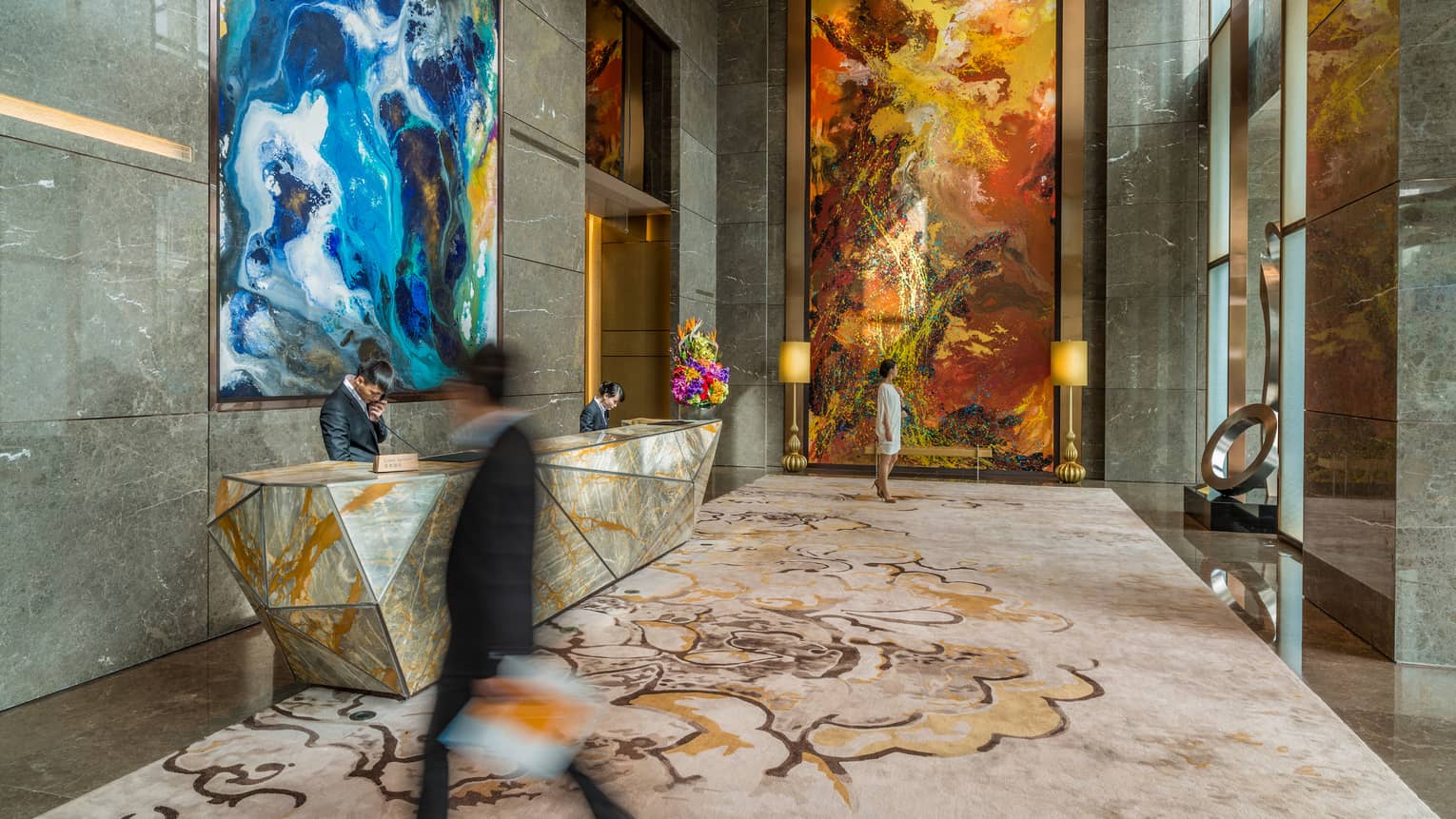 Man wearing suits walks through hotel lobby surrounded by marble, large modern art