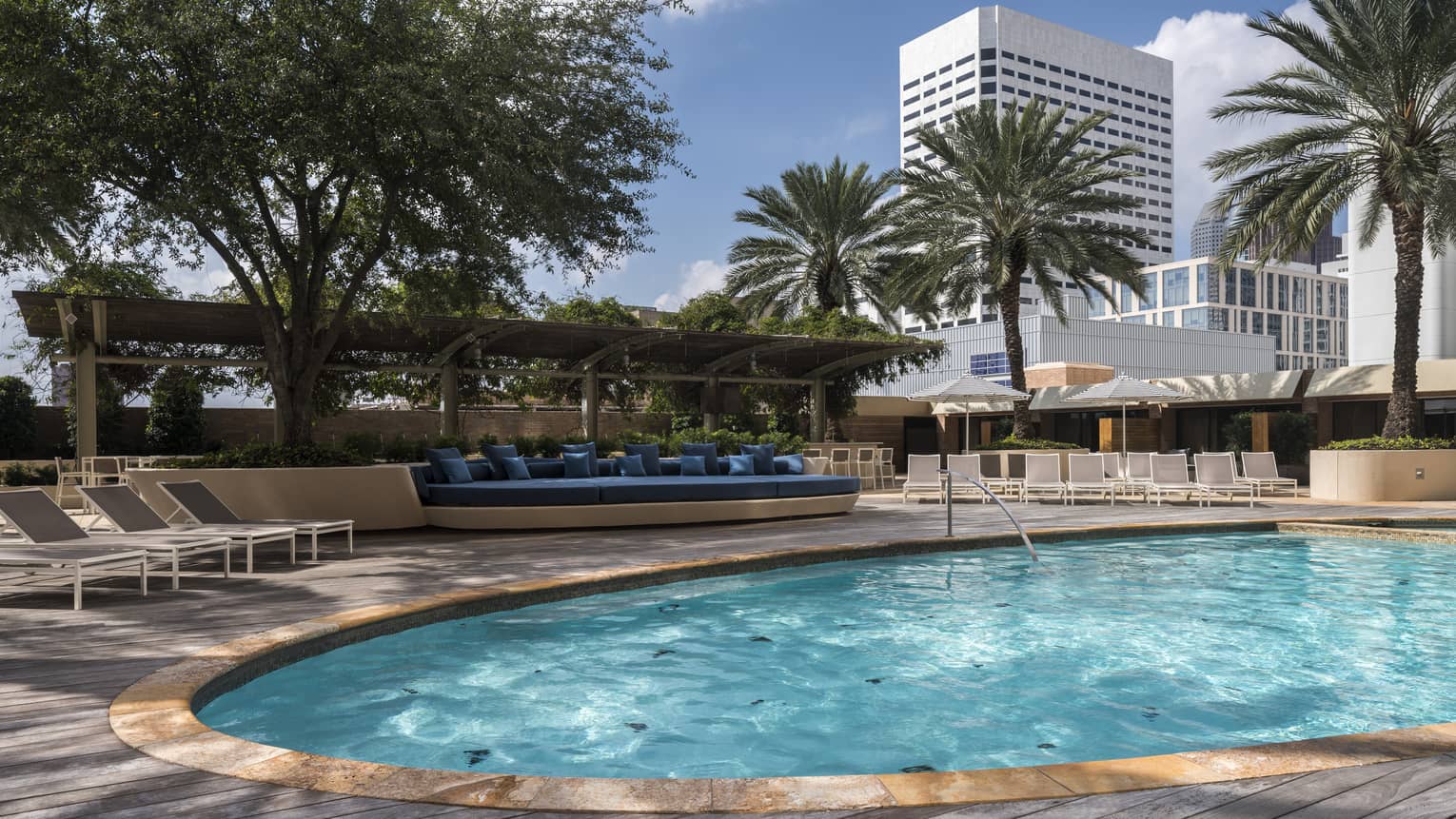 View across sunny outdoor swimming pool to patio, row of lounge chairs and palm trees