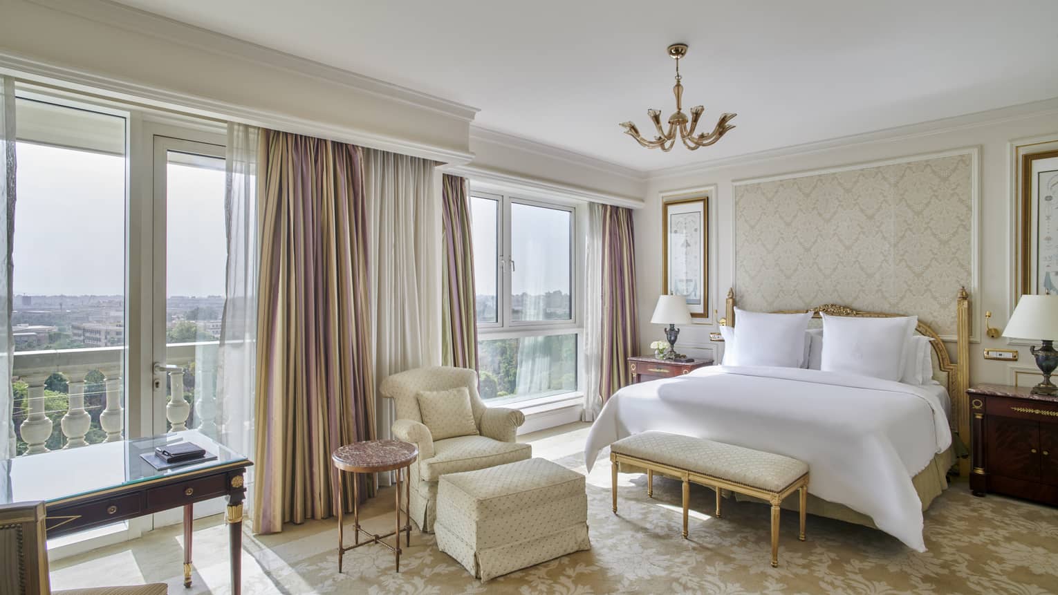 Guest room with king bed and white linens, foot bench, arm chair, floor-to-ceiling windows with city views