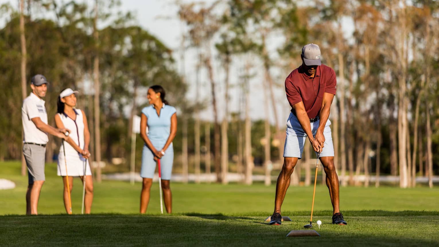 A man lines up a putt in the foreground while his wife and another couple laugh in the background at the golf course at four seasons orlando