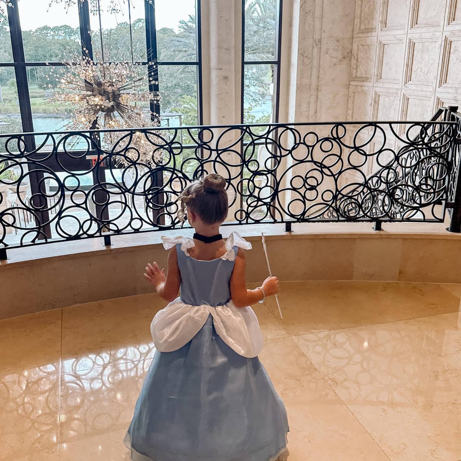 A young girl poses in a princess costume on a balcony overlooking a wall of glass windows