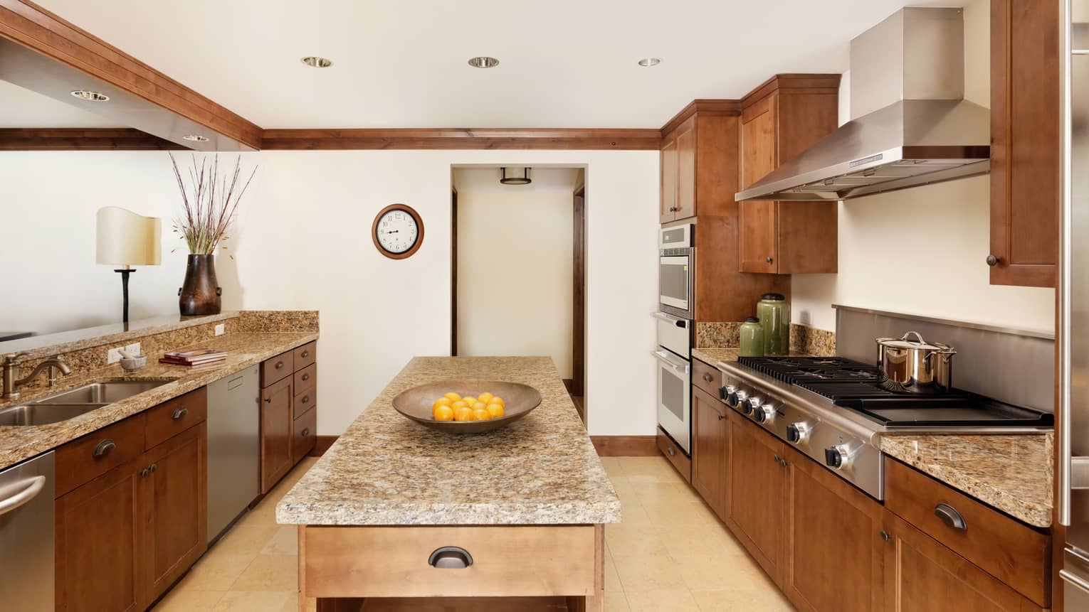 Luxury kitchen with granite countertops, wood cabinetry, large island with a bowl of fresh oranges, double ovens and stainless steel appliances