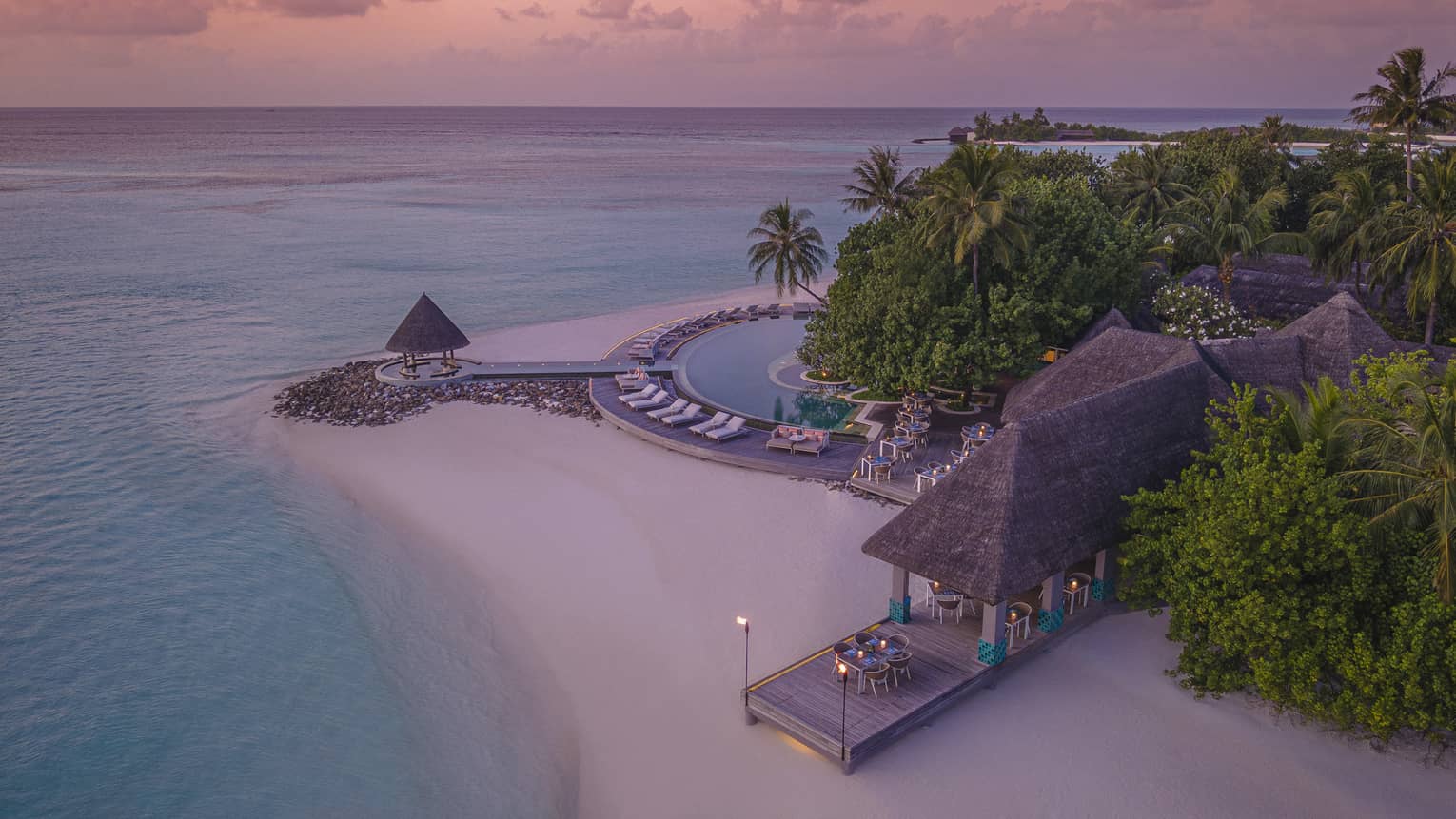 Aerial view of beachfront straw roof pavilion at sunset