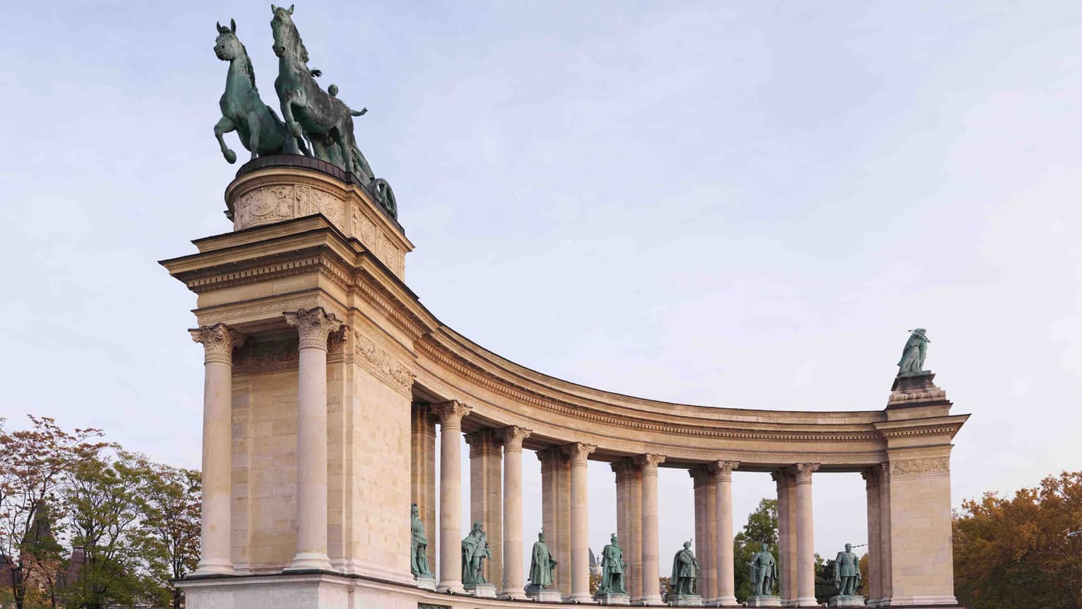 An intricately carved stone monument featuring columns and statues of armed figures, crowned by a statue of a chariot rider.