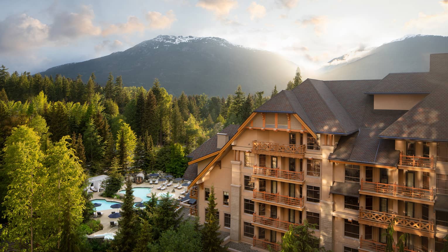 A large hotel building surrounded by mountains and trees during sunrise.