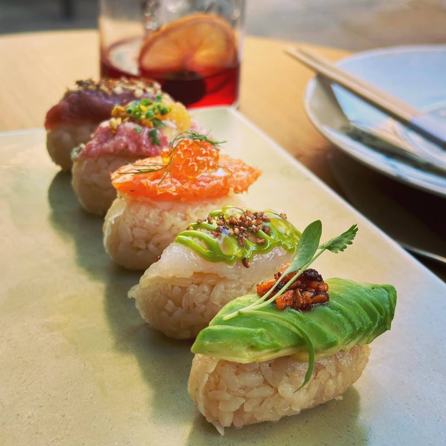 ,A plate of colorful sushi, served with a red cocktail
