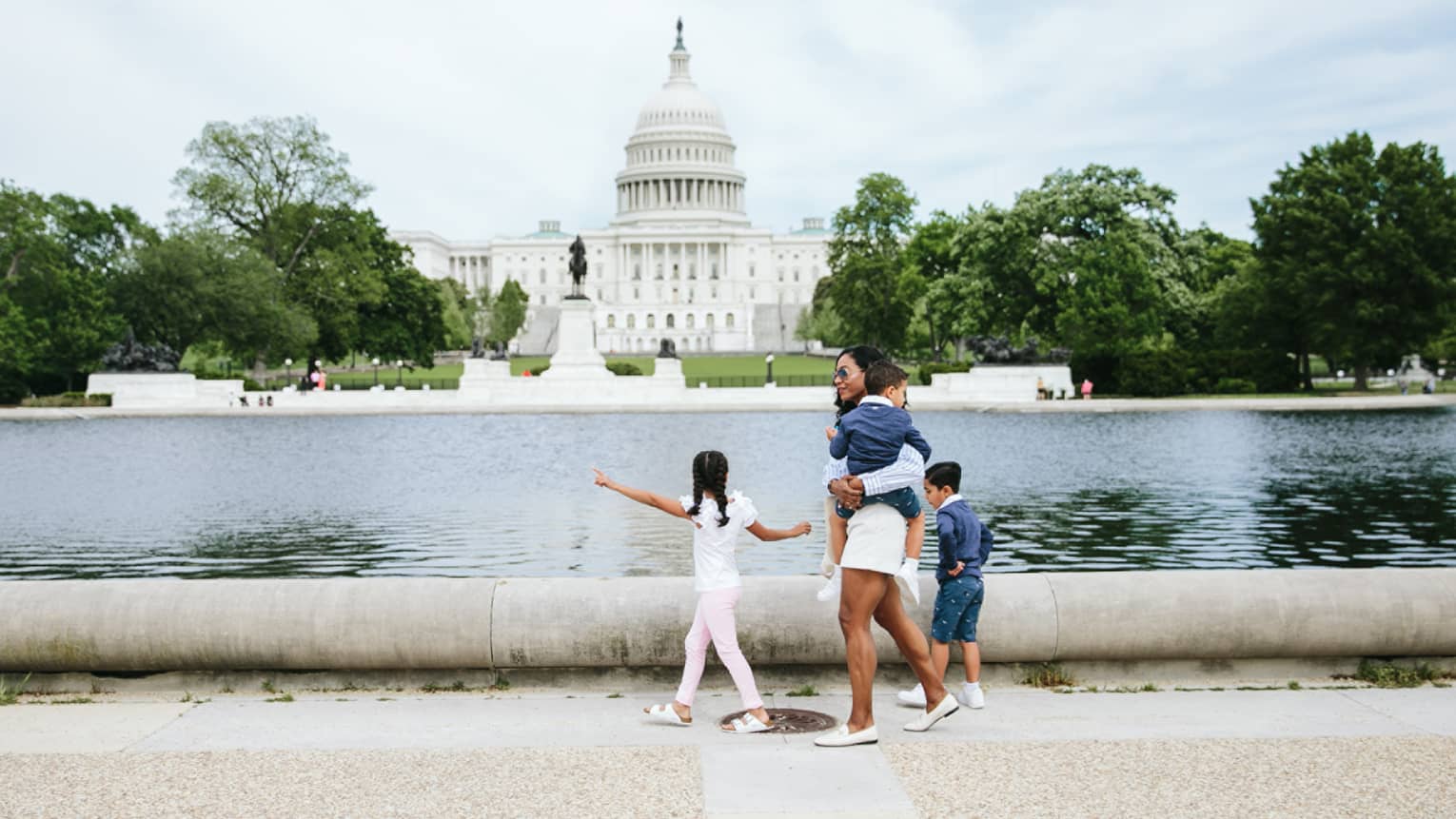 Woman and three children walk in front of the Capitol reflecting pool in Washington, DC, with Capitol building in background