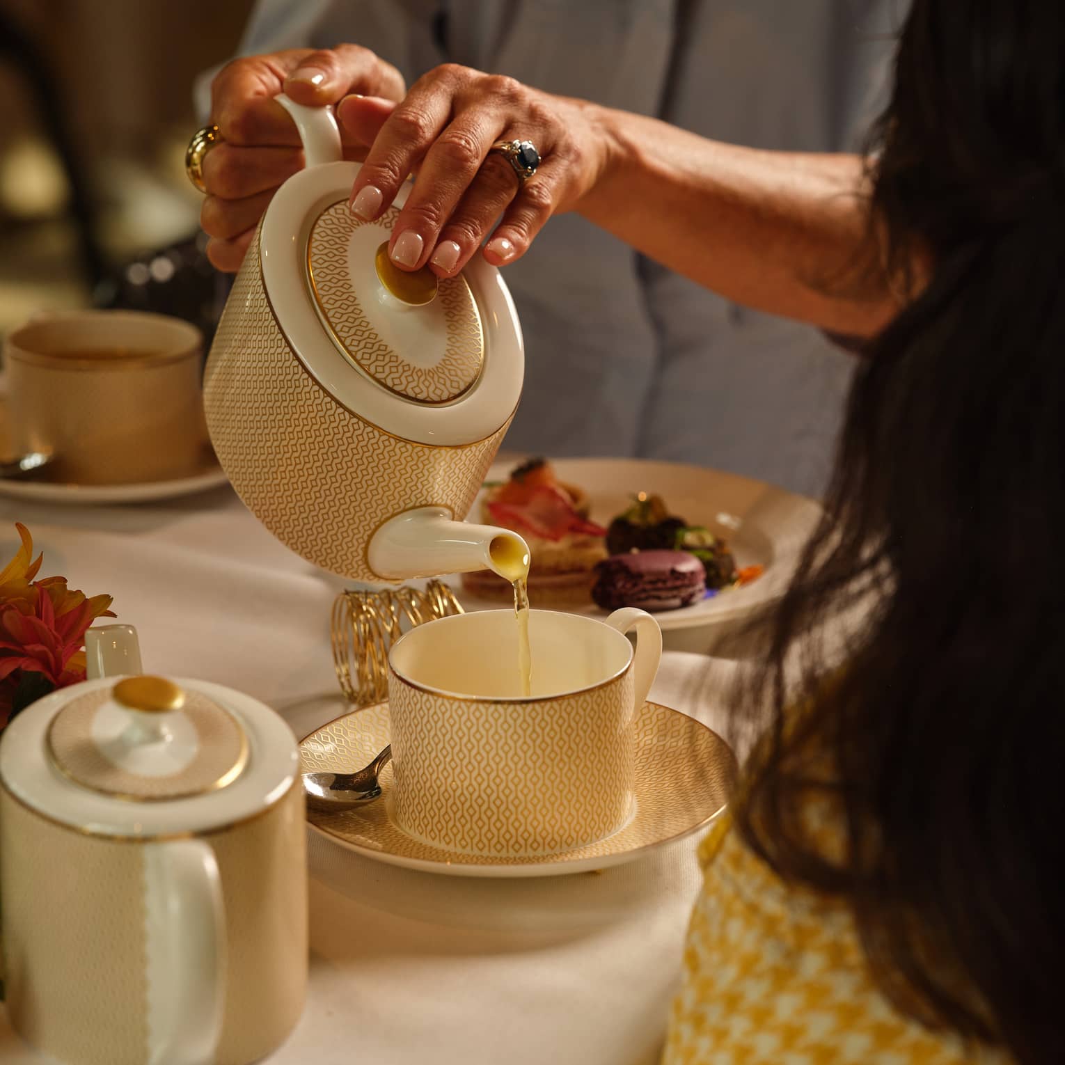 Person pours tea from a cream porcelain tea pot into a matching mug