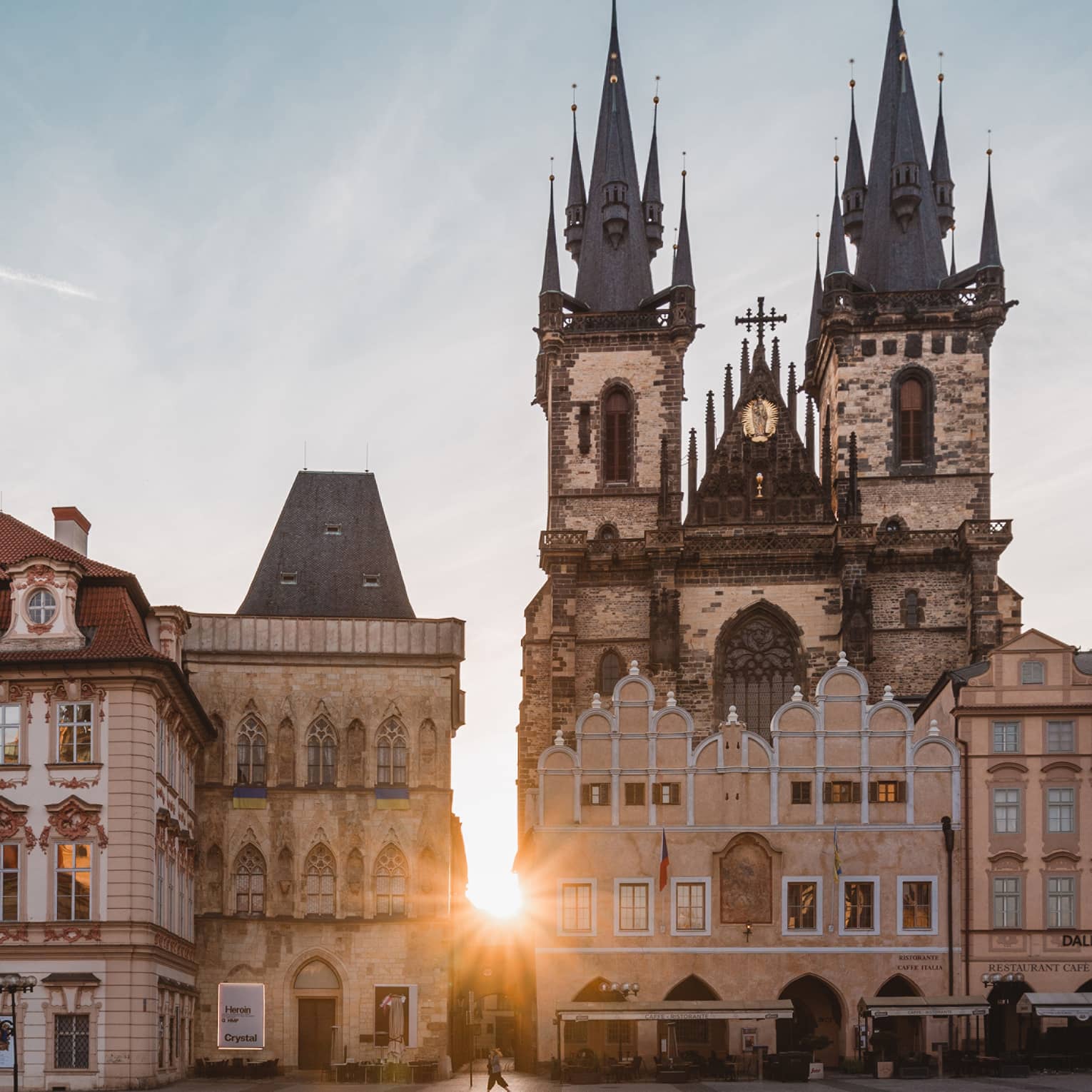 Sunset bursts through a medieval building with an intricate exterior and a formidable Gothic church with soaring spires.