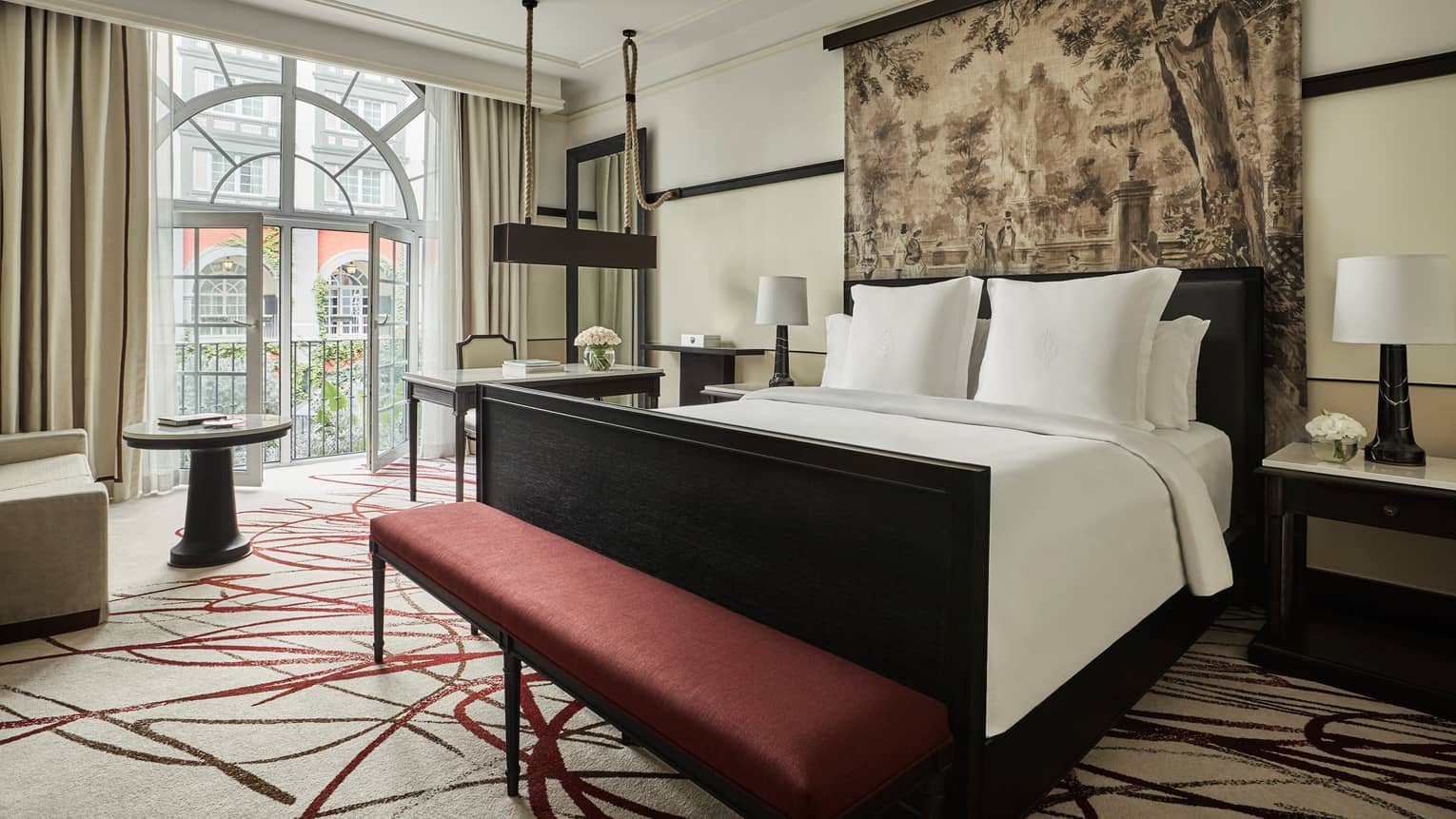Premier Room bed under print headboard, red bench at foot, sunny arched balcony glass doors