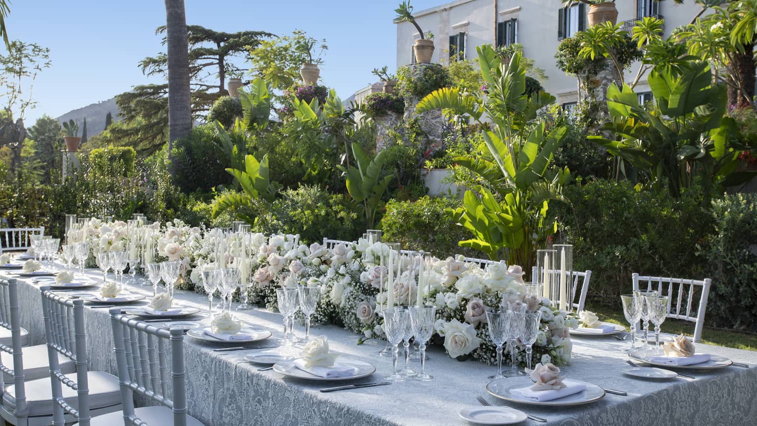 Elegantly set long table with extended floral wedding centrepiece alongside lush garden wall