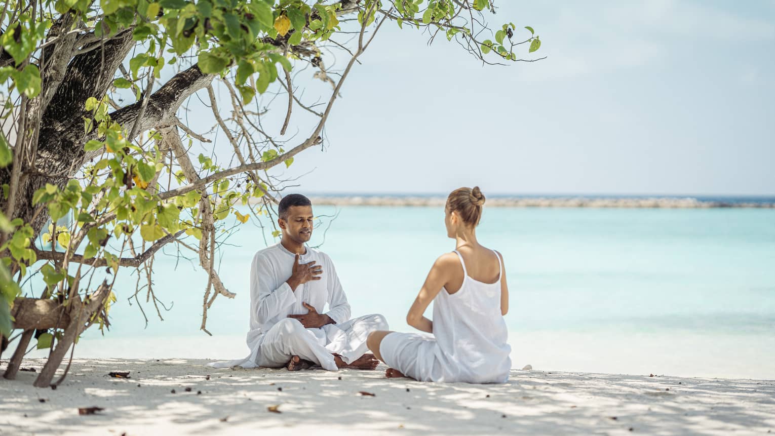 Dr. Arun K. Tomson practises breathing exercises with female guest on the beach under the shade of a tree
