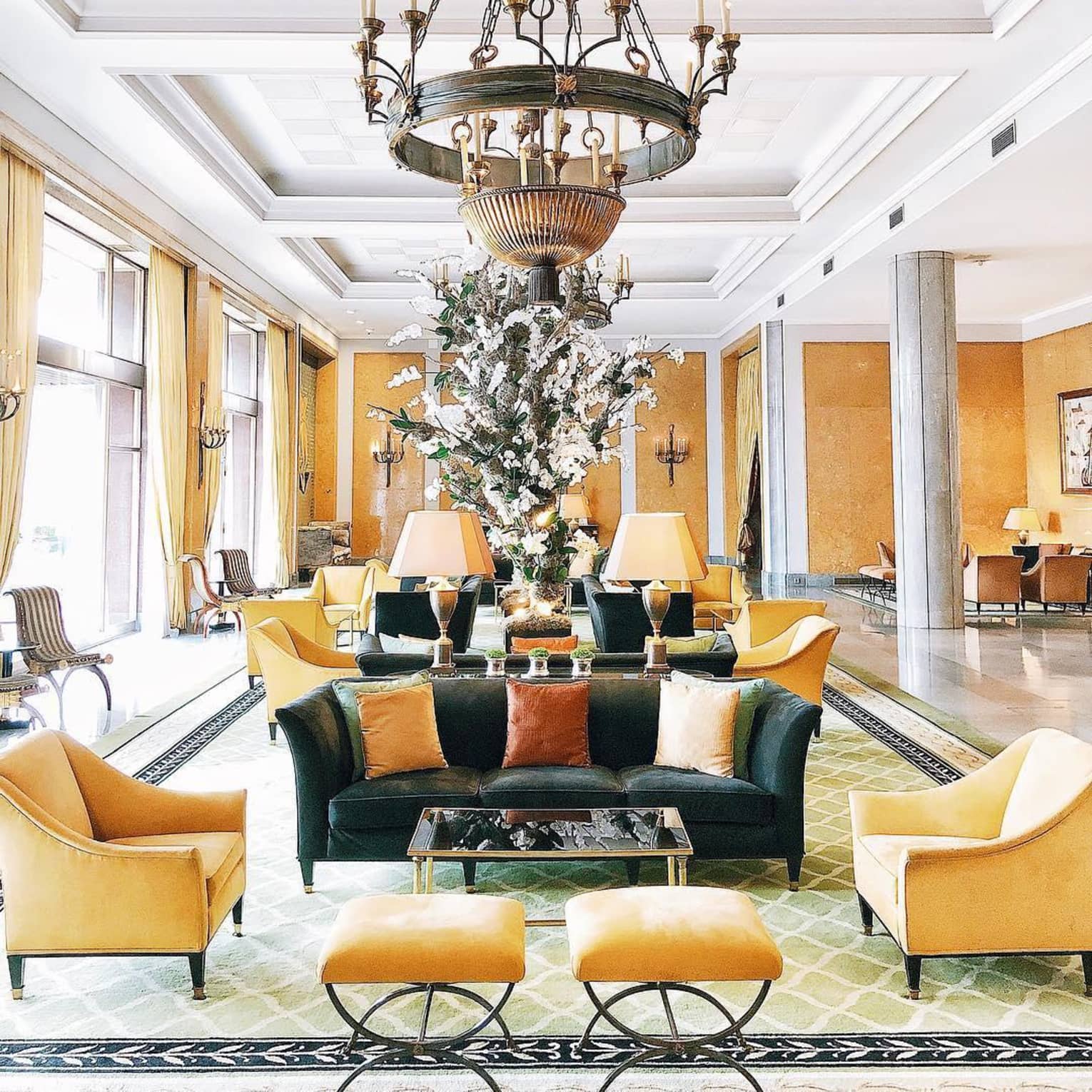 Chandelier over hotel lobby seating area with yellow chairs, footrests and curtains