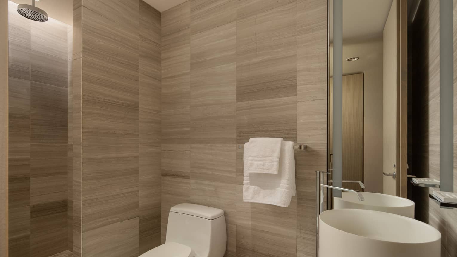 Hotel suite bathroom with a toilet, round sink, two towels on a rack and rain shower head