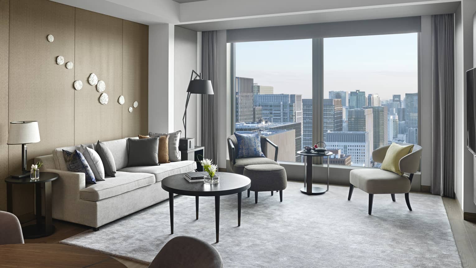Stylish living room with a grey sofa, armchairs, lamps, round tables and large windows offering city views