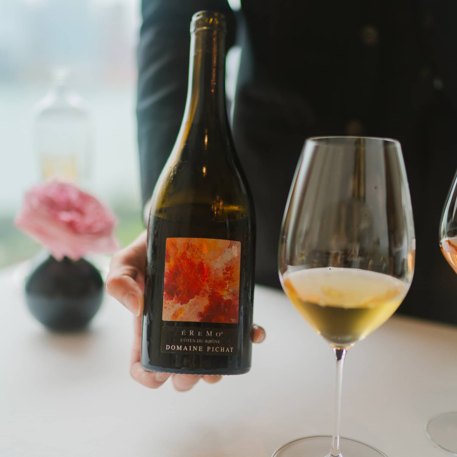 Person holding a wine bottle beside a glass of wine.
