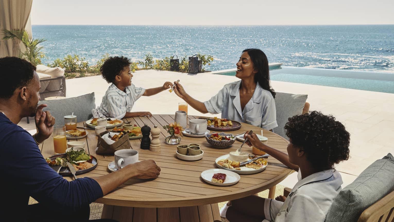 Family enjoying breakfast together at a round wooden table on an ocean-view terrace at a luxury resort
