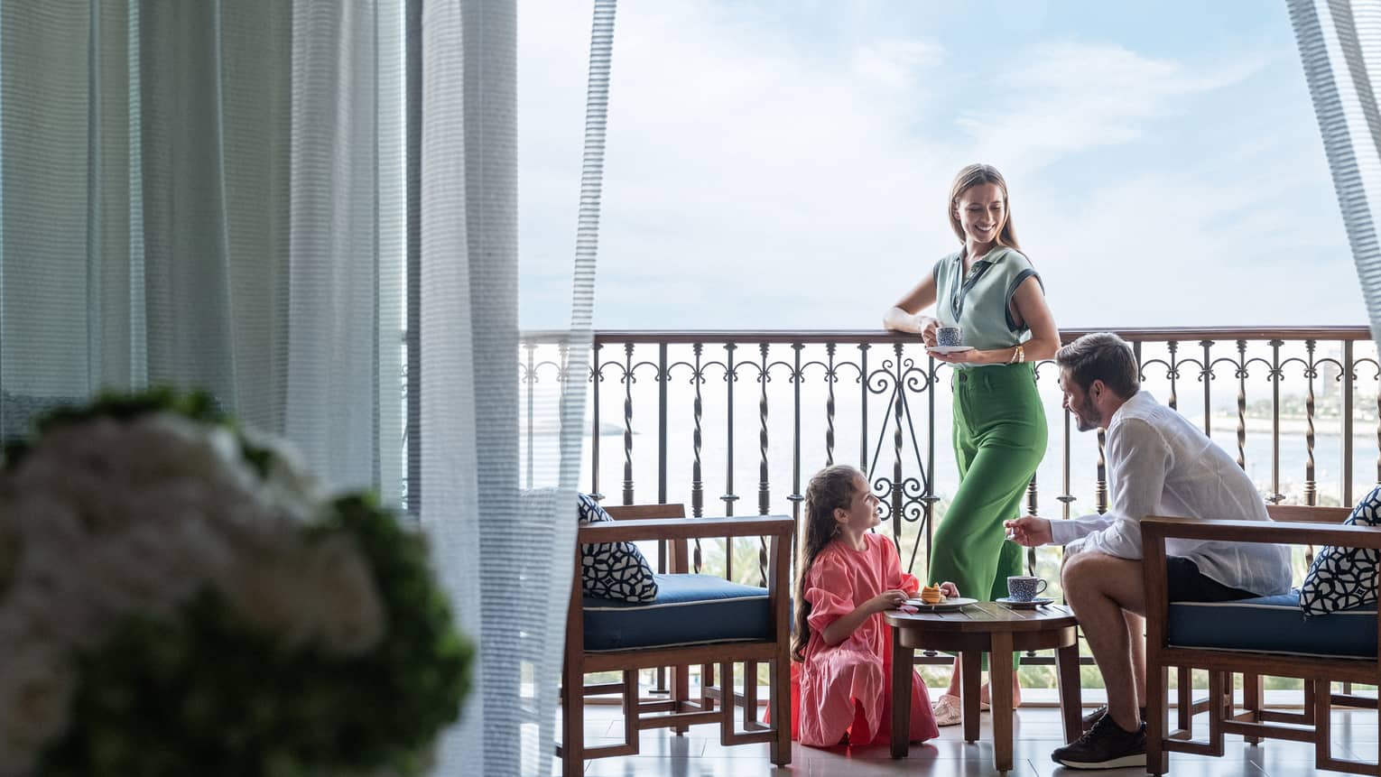 A couple and their daughter stand on a balcony below a bright blue sky.